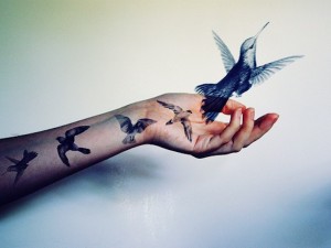 arm tattooed with birds holds a bird that's about to fly away