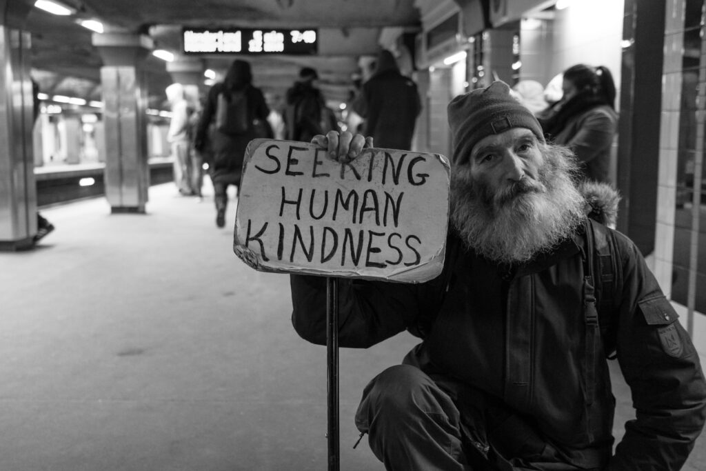 elderly man holding sign that reads seeking human kindness, photo by Matt Collamer via upsplash.com