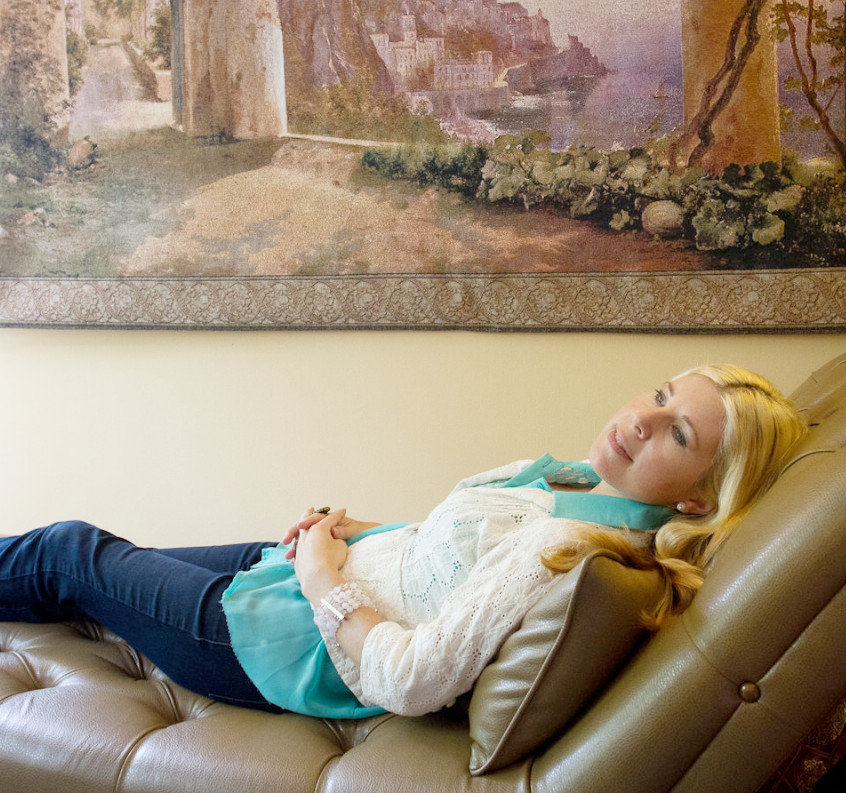 a blond woman lying on a psychiatrist's couch with a painting hanging on the wall above her
