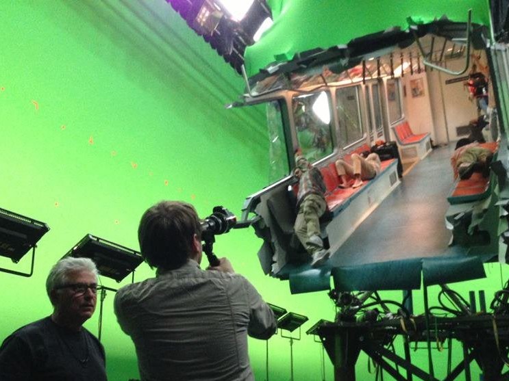 a film crew in a green room pointing their cameras at a full color picrture of the interior of a subway car